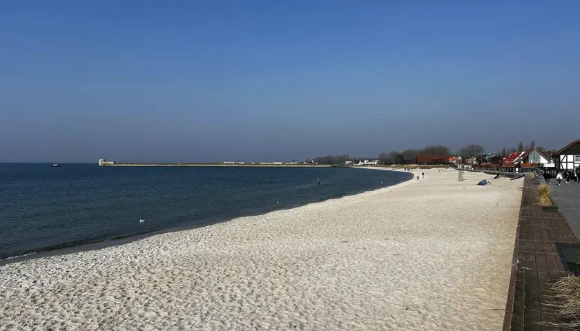 Piękna plaża, idealna na rejs z Gdańska na Hel. W oddali widać falochron i zabudowania.