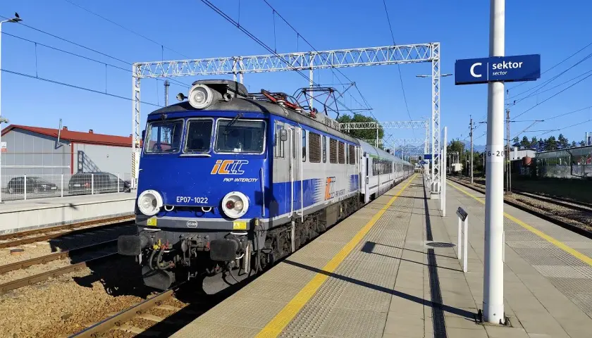 Niebiesko-szary pociąg PKP Intercity EP07-1022 stoi na peronie. Zastanawiasz się, ile jedzie pociąg z Poznania do Krakowa?