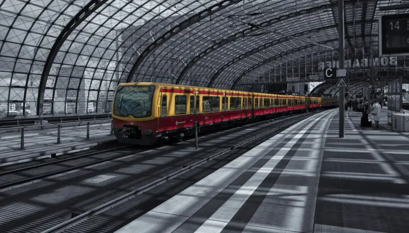 Żółto-czerwony pociąg S-Bahn Berlin stoi na nowoczesnym, zadaszonym peronie.
