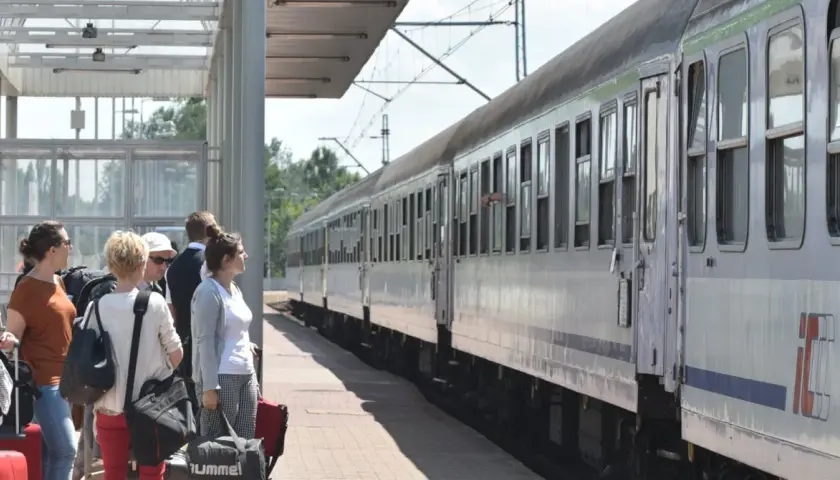 Ludzie z bagażami czekają na pociąg PKP. Zastanawiasz się, kto ma zniżki na PKP? Sprawdź ofertę przewoźnika!