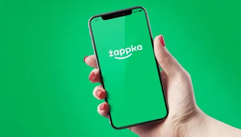 Dłoń trzyma smartfon z zielonym ekranem i logo Żappka. Sprawdzam, czy w Żabce są bilety autobusowe.