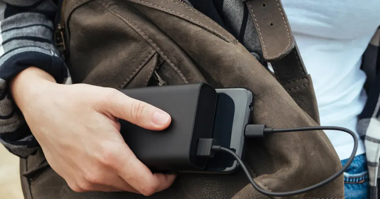 Ręka trzyma powerbank ładujący telefon. Podróżując, warto wiedzieć, czy w pociągu można ładować telefon.