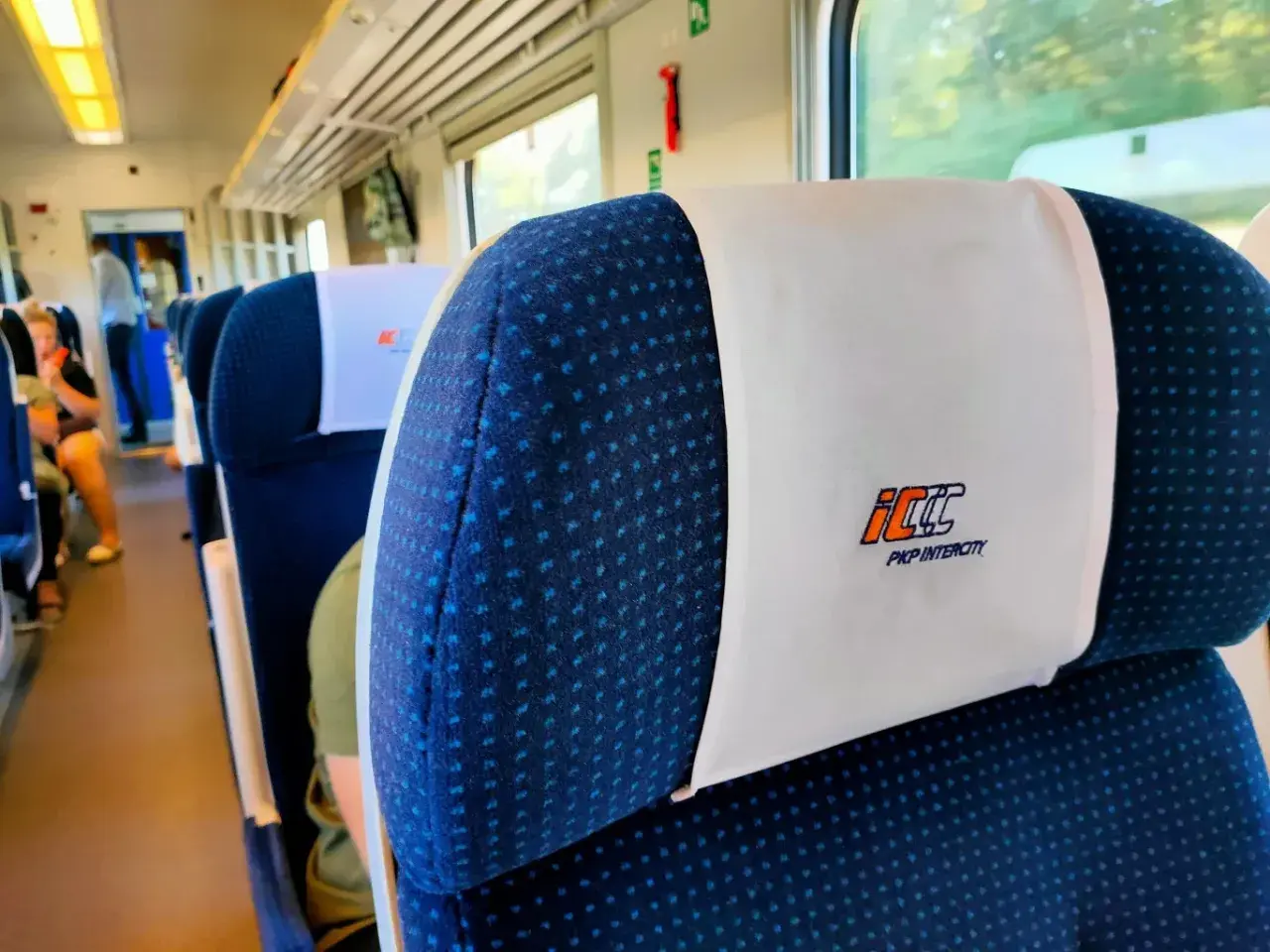 Wnętrze pociągu PKP Intercity. Siedzenia z zagłówkami, na których widnieje logo przewoźnika. Czy bilet PKP z rezerwacją miejsca czy bez – kiedy warto dopłacić?