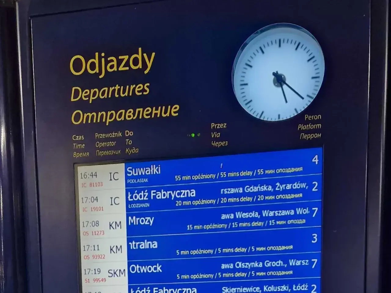 Tablica odjazdów pociągów pokazuje, gdzie sprawdzić opóźnienia pociągu. Widoczne są czasy, kierunki i informacje o opóźnieniach.