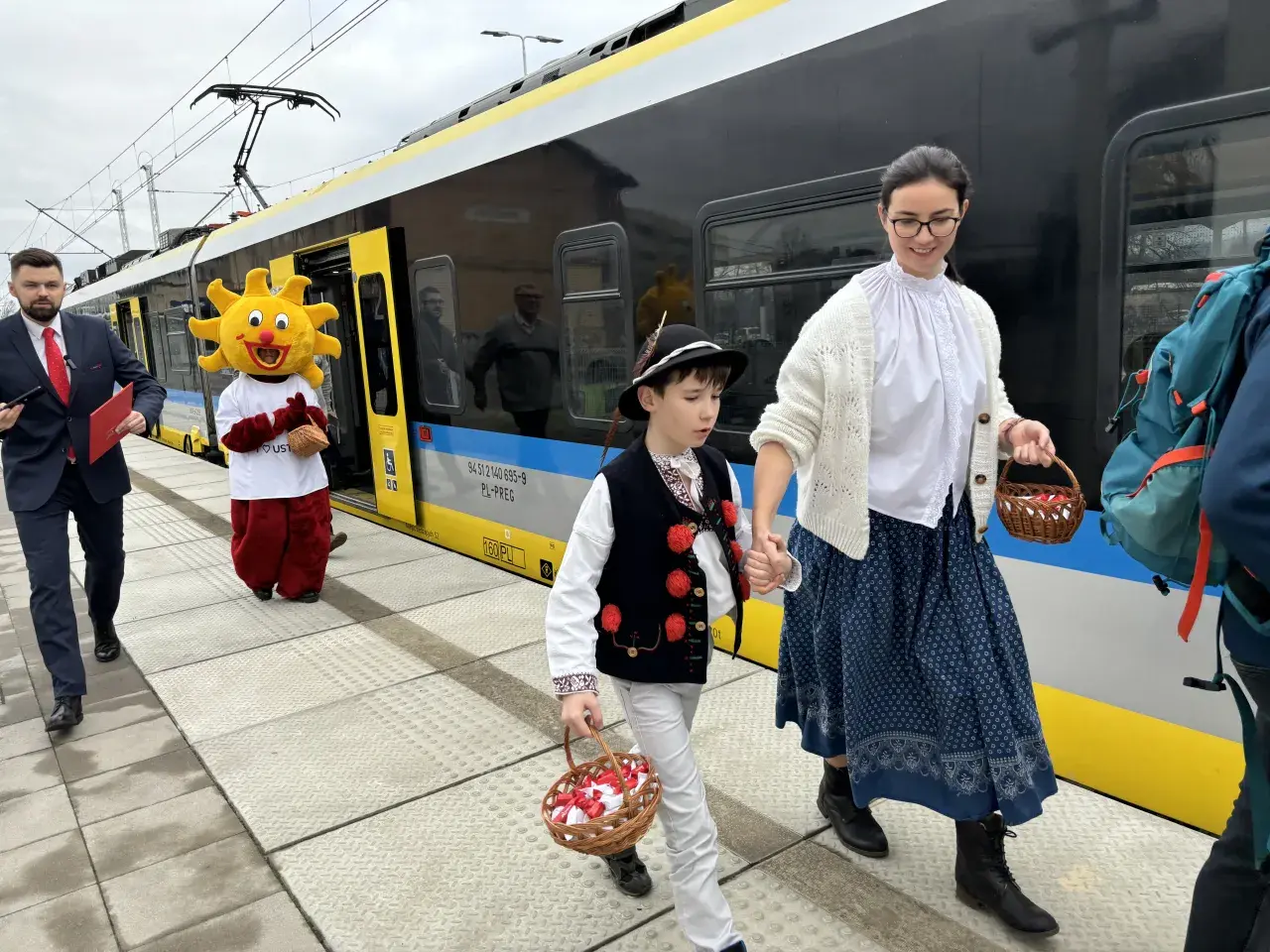 Ludzie w strojach ludowych i Słońce idą na peron, by dowiedzieć się, jak dojechać do Ustronia Górskiego.