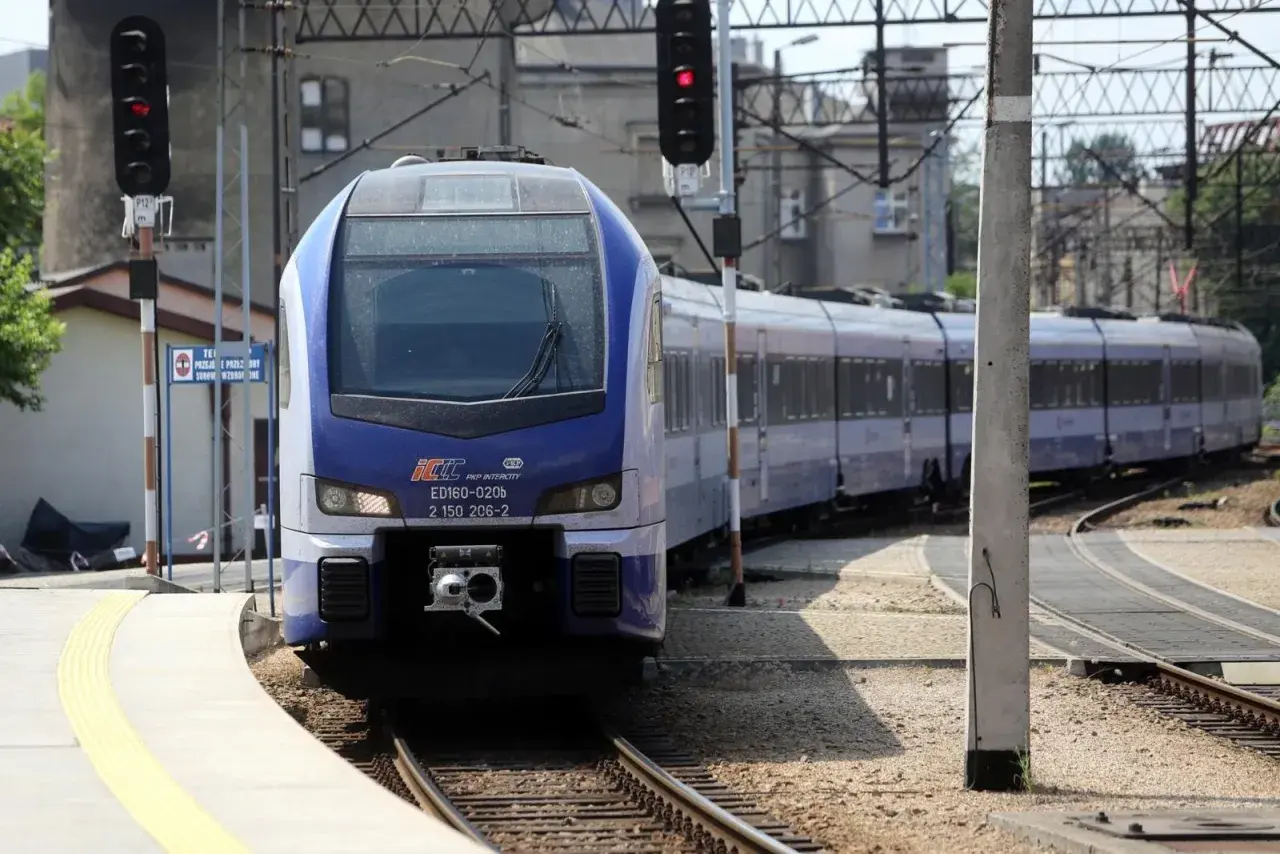 Niebiesko-biały pociąg PKP Intercity ED160-020b na torach, z sygnalizacją świetlną.