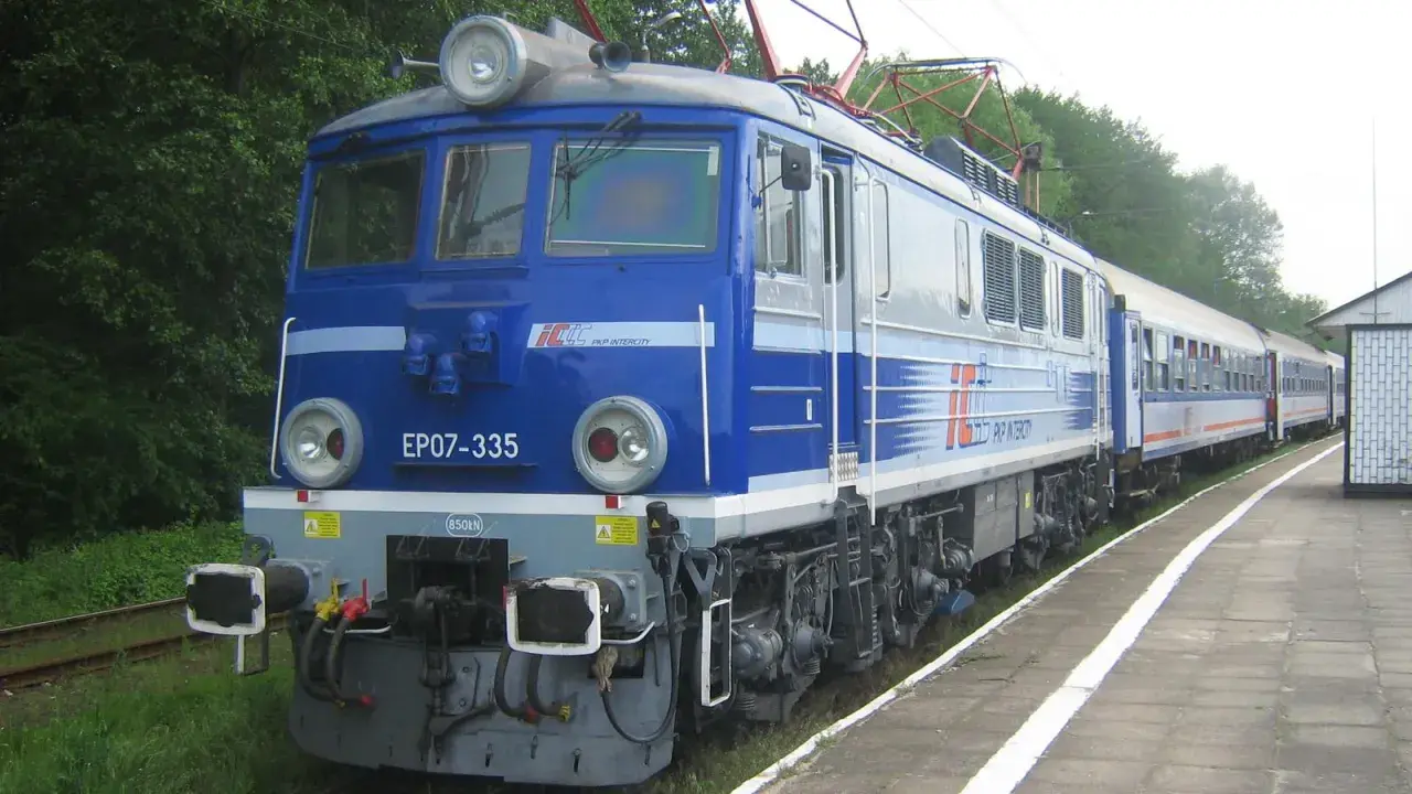 Niebieska lokomotywa EP07-335 PKP Intercity z pociągiem pasażerskim na stacji.