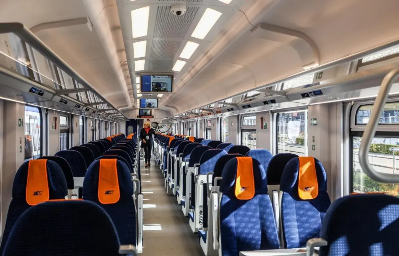 Wnętrze nowoczesnego wagonu PKP Intercity. Siedzenia w kolorze granatowym z pomarańczowymi zagłówkami. Ile wagonów ma pociąg IC? To zależy od trasy i typu składu.