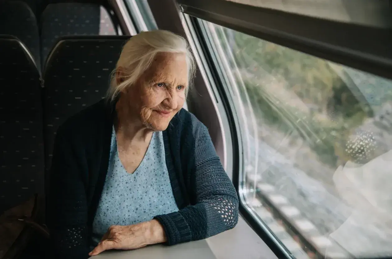 Starsza pani wpatruje się w krajobraz za oknem pociągu Pendolino, zastanawiając się, czy na pendolino są zniżki dla emerytów.