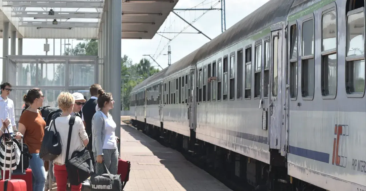 Ludzie czekają na pociąg PKP. Zastanawiają się, ile wynosi zniżka uczniowska PKP, by podróżować taniej.