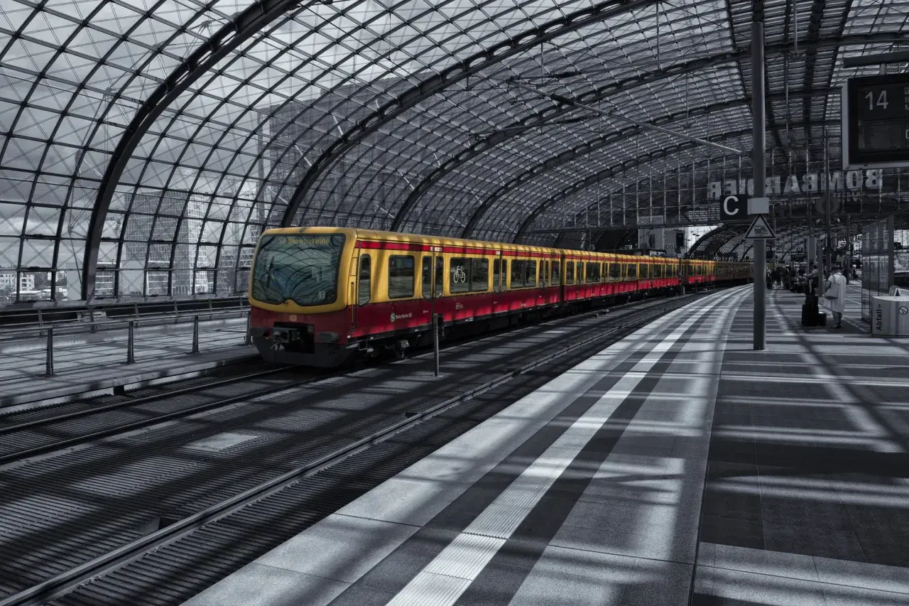 Żółto-czerwony pociąg S-Bahn Berlin stoi na nowoczesnym, zadaszonym peronie.