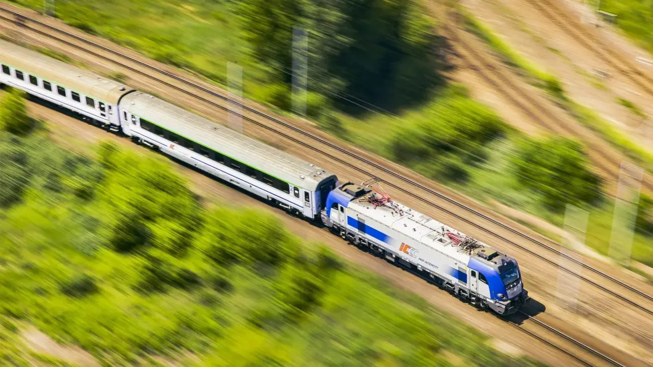Pociąg PKP Intercity pędzi przez zielone krajobrazy. Chcesz wiedzieć, jak dokupić rezerwację miejsca do kupionego już biletu?