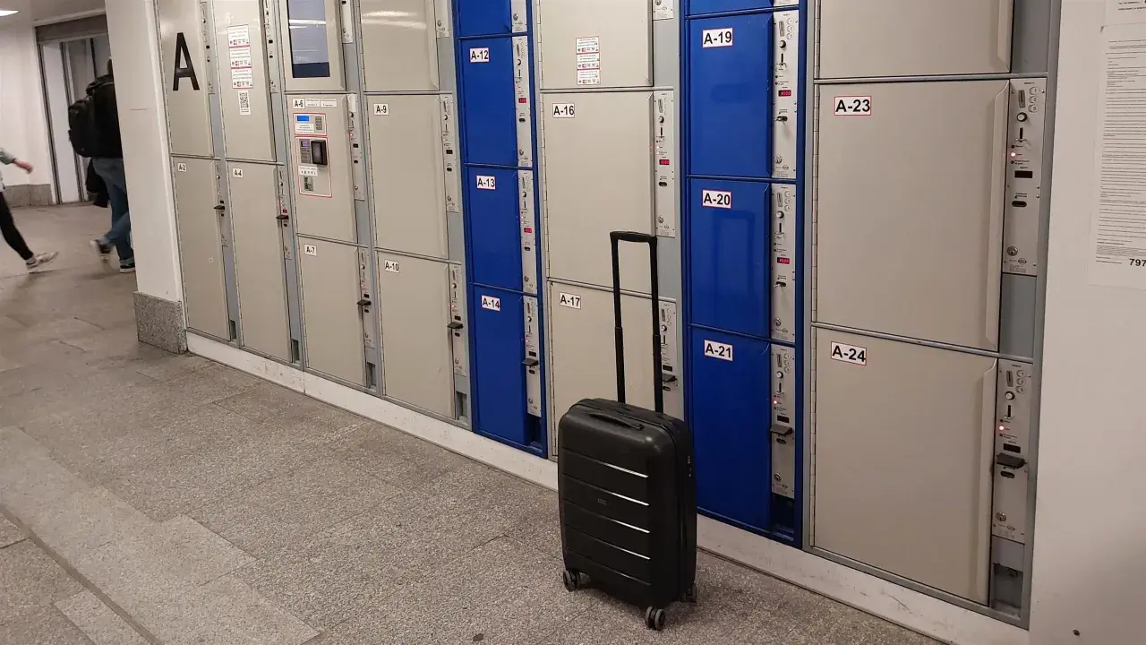 Na Dworcu Warszawa Centralna jest przechowalnia bagażu. Widać rzędy skrytek bagażowych, a obok jedna czarna walizka.