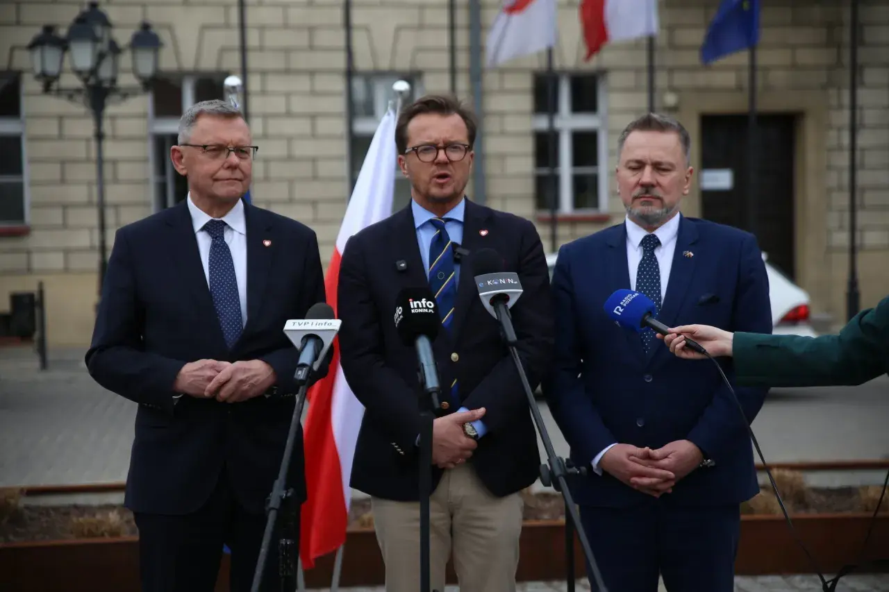 Trzech mężczyzn w garniturach przemawia do mikrofonów. W tle flagi Polski i Unii Europejskiej.