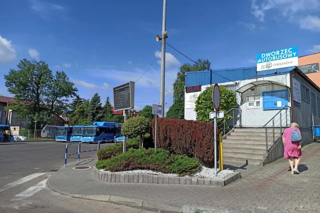 Chrzanów dworzec autobusowy. Niebieskie autobusy czekają na pasażerów, a kobieta w różowej sukience idzie w stronę budynku.
