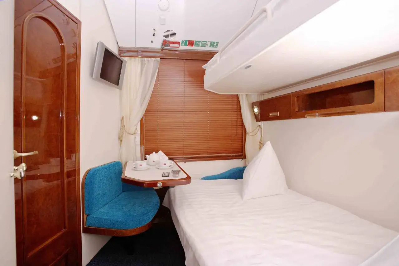 Wnętrze wagonu sypialnego Pendolino z łóżkiem, niebieską kanapą, stolikiem z herbatą i telewizorem.