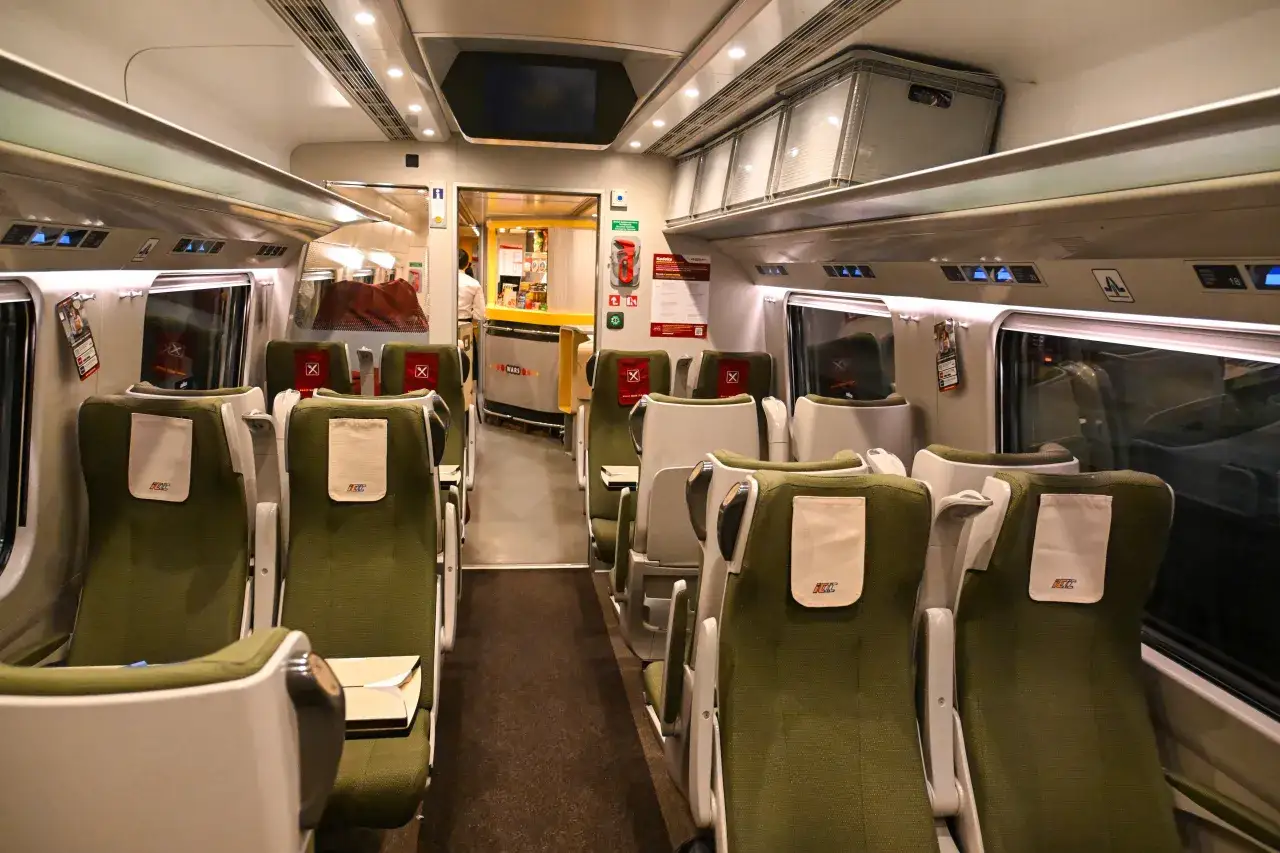 Wnętrze pociągu Pendolino, zielone fotele i stoliki. Podróż z Krakowa do Warszawy tym szybkim pociągiem to komfort.