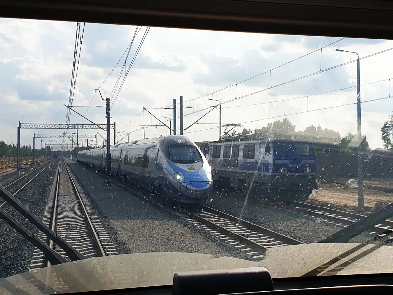 Widok z kabiny maszynisty na torach, gdzie widać, jak szybko jedzie pendolino obok lokomotywy.