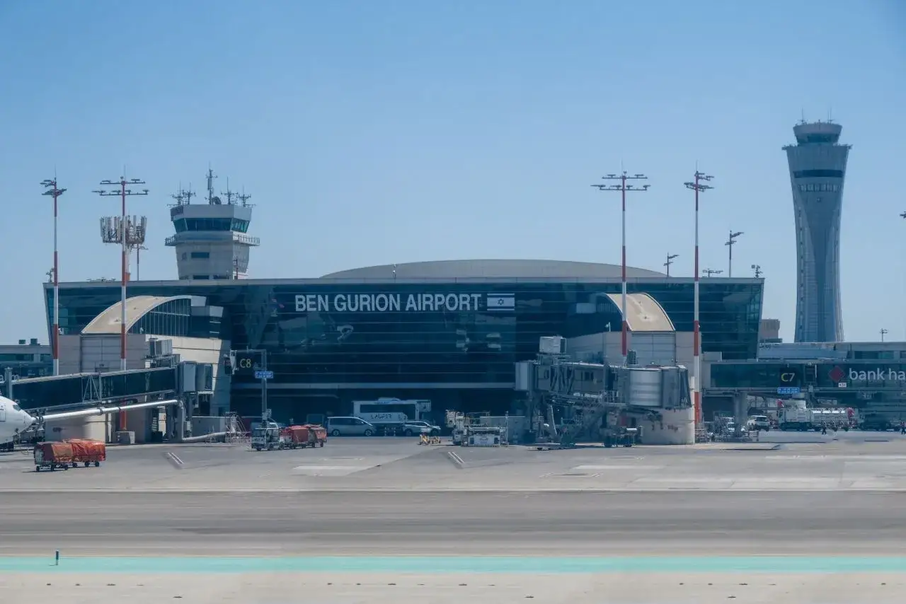 Nowoczesny terminal lotniska Ben Gurion z wieżą kontroli lotów i samolotami na płycie lotniska.