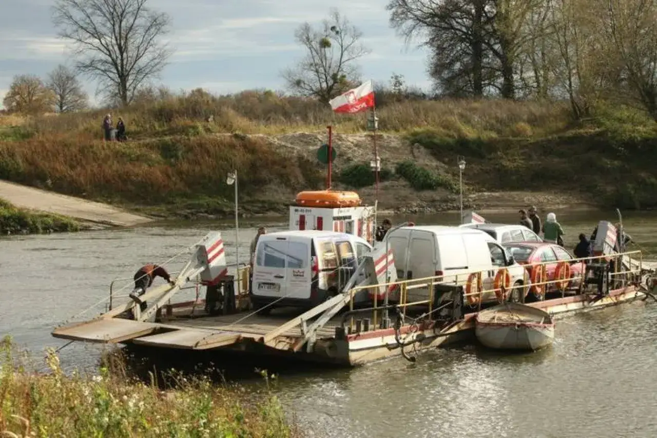Przeprawa promowa na Zalew Prężyce przewozi samochody i ludzi. Na promie białe vany i czerwony samochód.