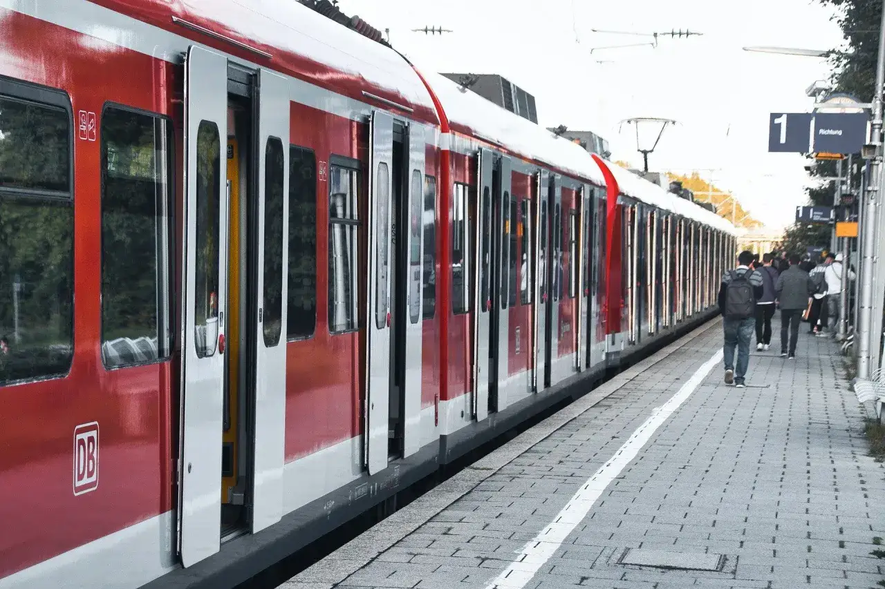 Czerwony pociąg DB na peronie, ludzie czekają na podróż. Może to czas na wymiana biletu?