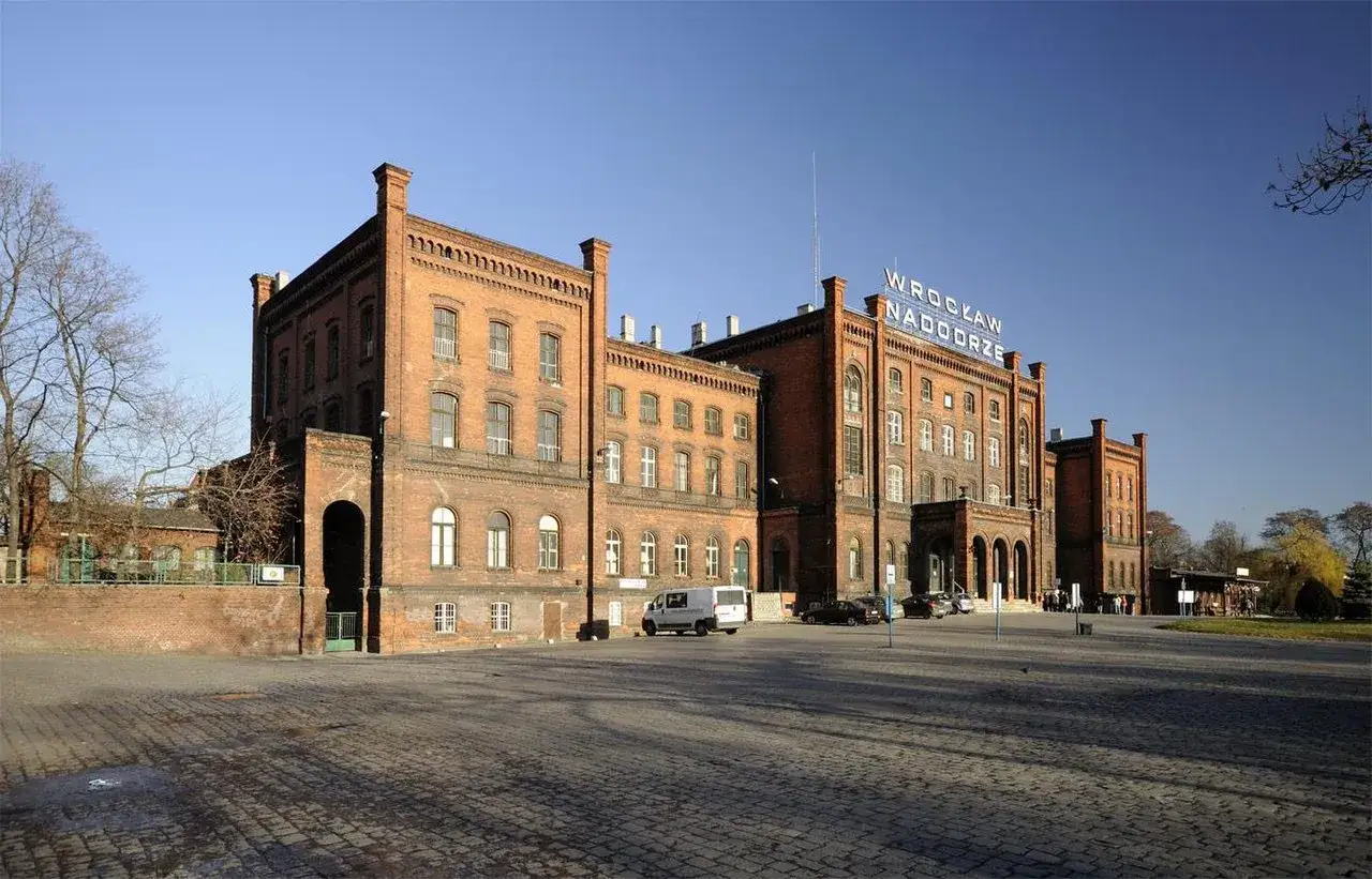 Dawny dworzec Wrocław Nadodrze PKP, ceglany budynek z charakterystycznym napisem, stoi na brukowanym placu.