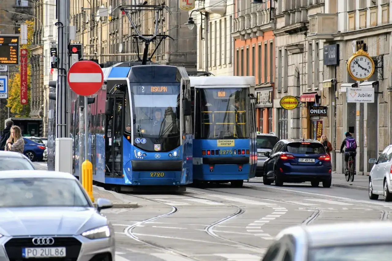 Dwa niebieskie tramwaje jadą ulicą w Krakowie. Zastanawiasz się, ile jest z dworca na rynek?