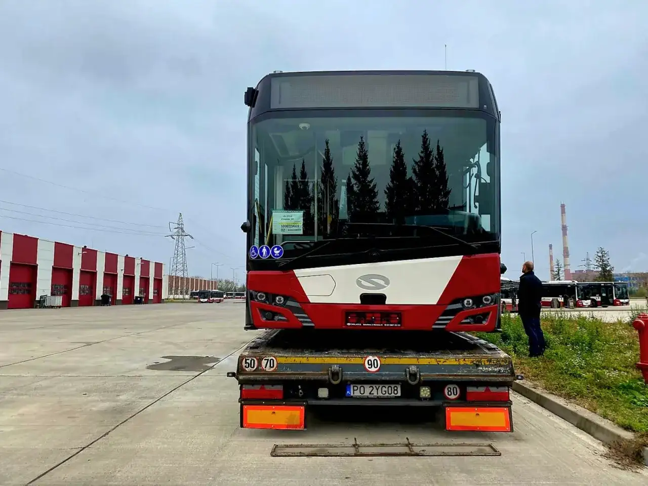 Nowy autobus czeka na transport z mzk zajezdnia autobusowa. W tle inne pojazdy i budynki.