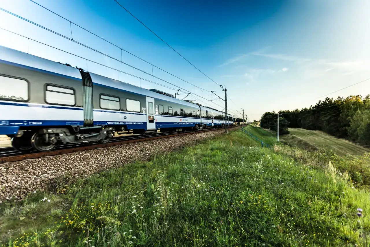 Pociąg Intercity pędzi przez zielone pola. Dowiedz się, jak połączyć się z wifi Intercity, by podróżować komfortowo.