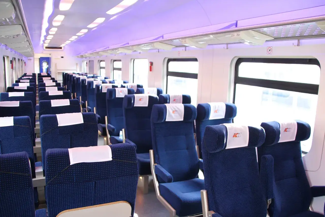 Wnętrze nowoczesnych intercity wagonów bez przedziałów. Rzędy niebieskich foteli z białymi zagłówkami czekają na pasażerów.