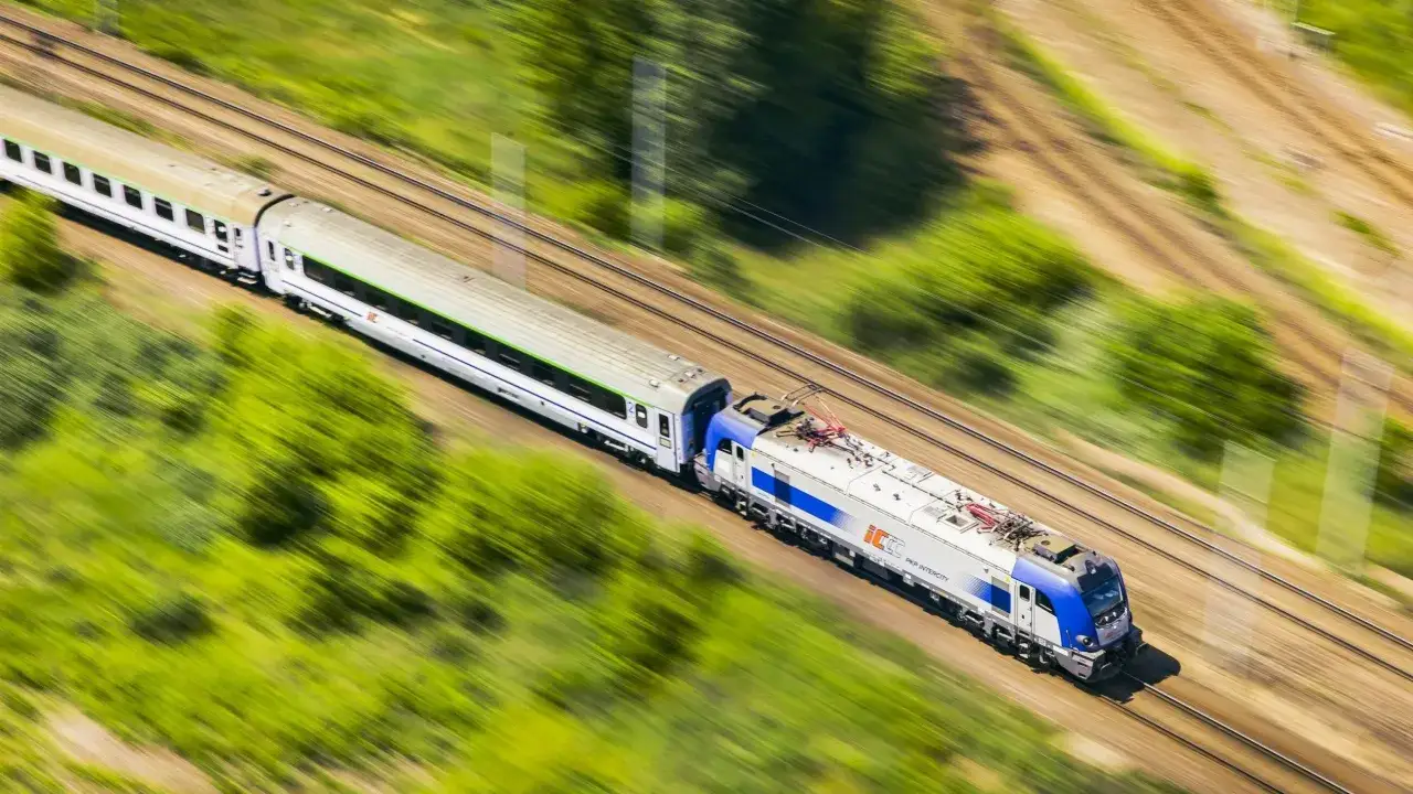 Pociąg PKP Intercity mknie przez zielone krajobrazy. Chcesz wiedzieć, jak sprawdzić wolne miejsca w pociągu?