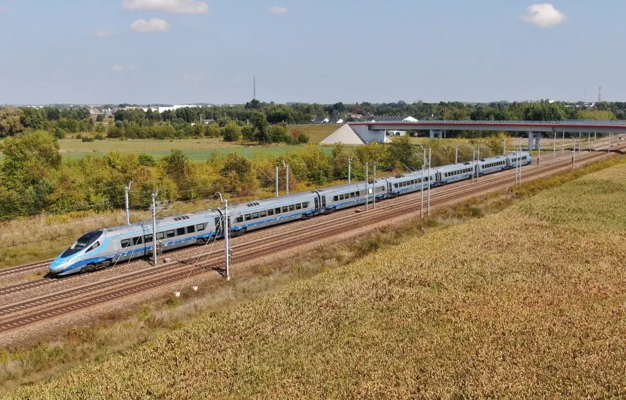 Srebrno-niebieski pociąg Pendolino pędzi po torach przez pola i lasy, pokazując, jak szybko jedzie Pendolino.