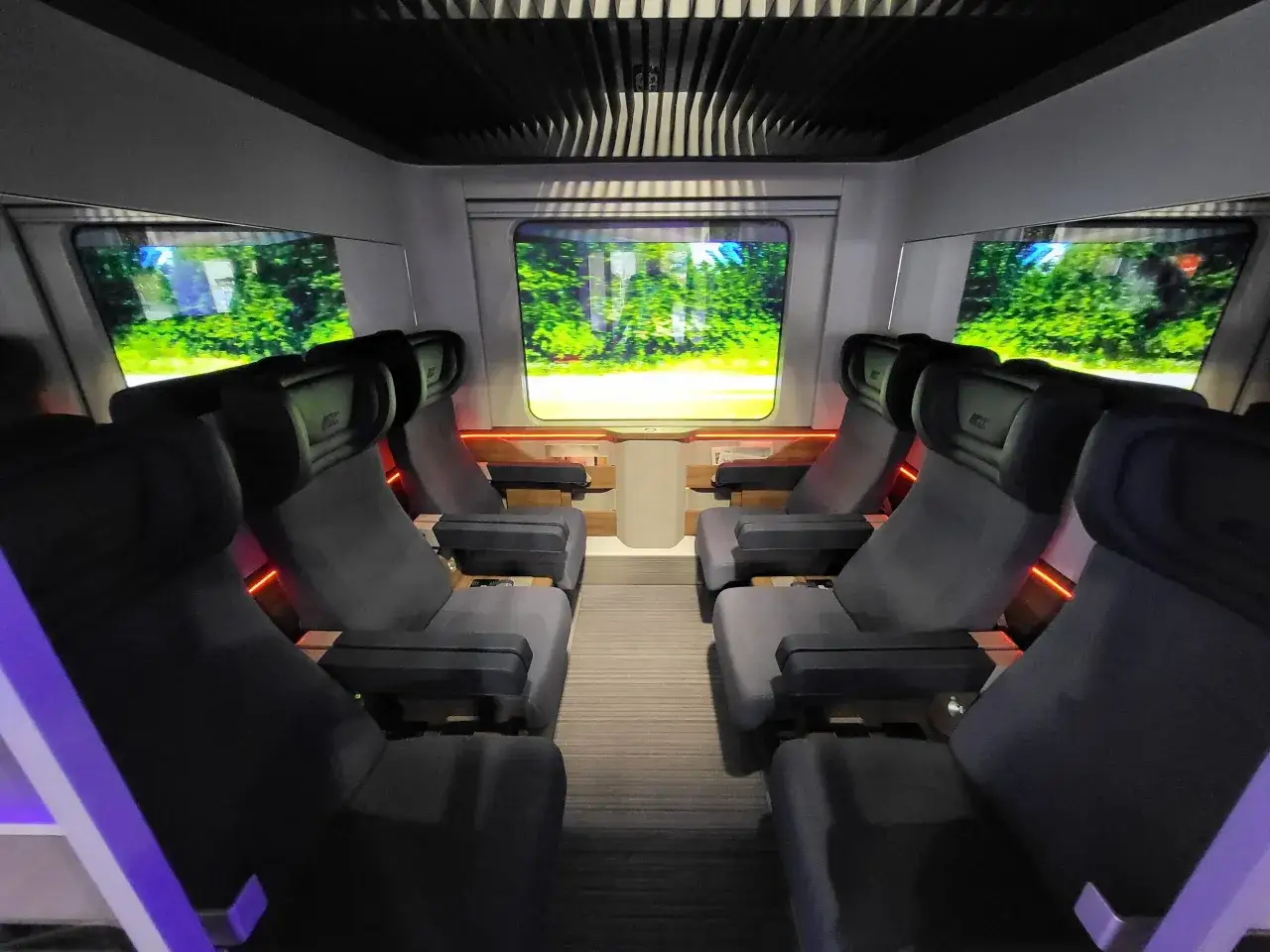 Wnętrze nowoczesnego pociągu Intercity z wygodnymi fotelami i ekranami imitującymi widok za oknem.