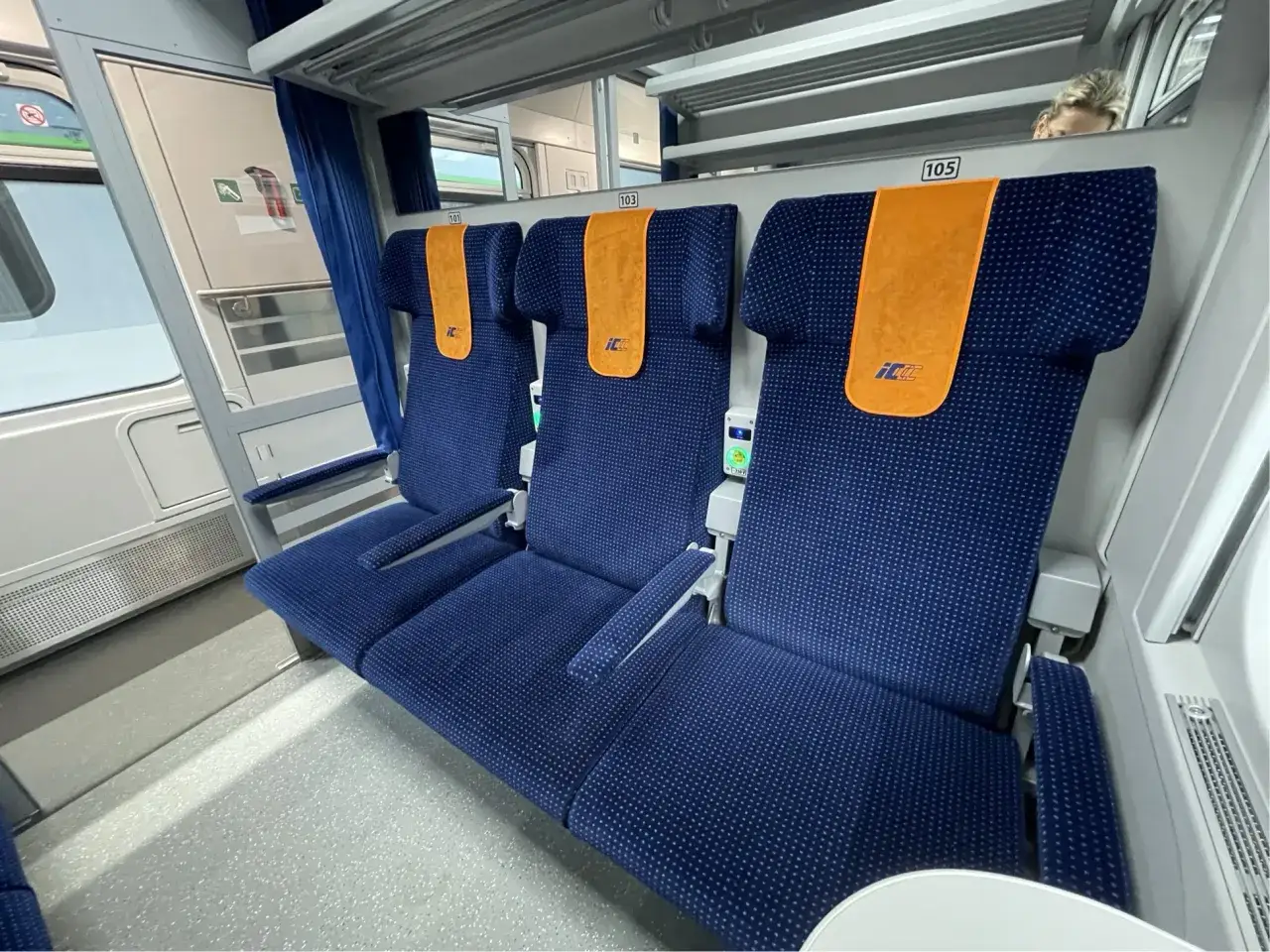 Wnętrze pociągu PKP Intercity z rzędami niebieskich foteli. Nie wiadomo, ile wagonów ma pociąg IC.