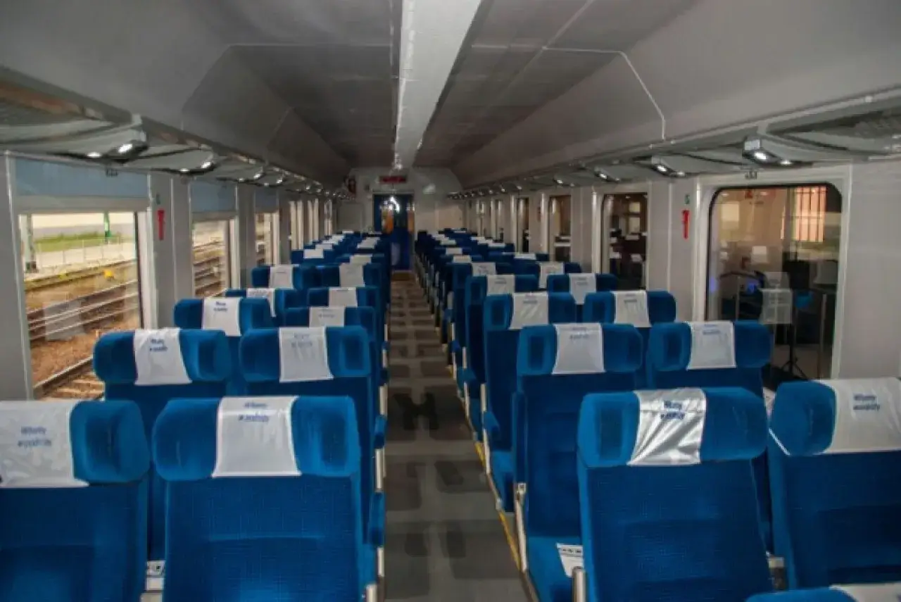 Wnętrze pociągu Intercity z rzędami niebieskich, wygodnych siedzeń. Wagony bez przedziałów oferują przestronne podróżowanie.