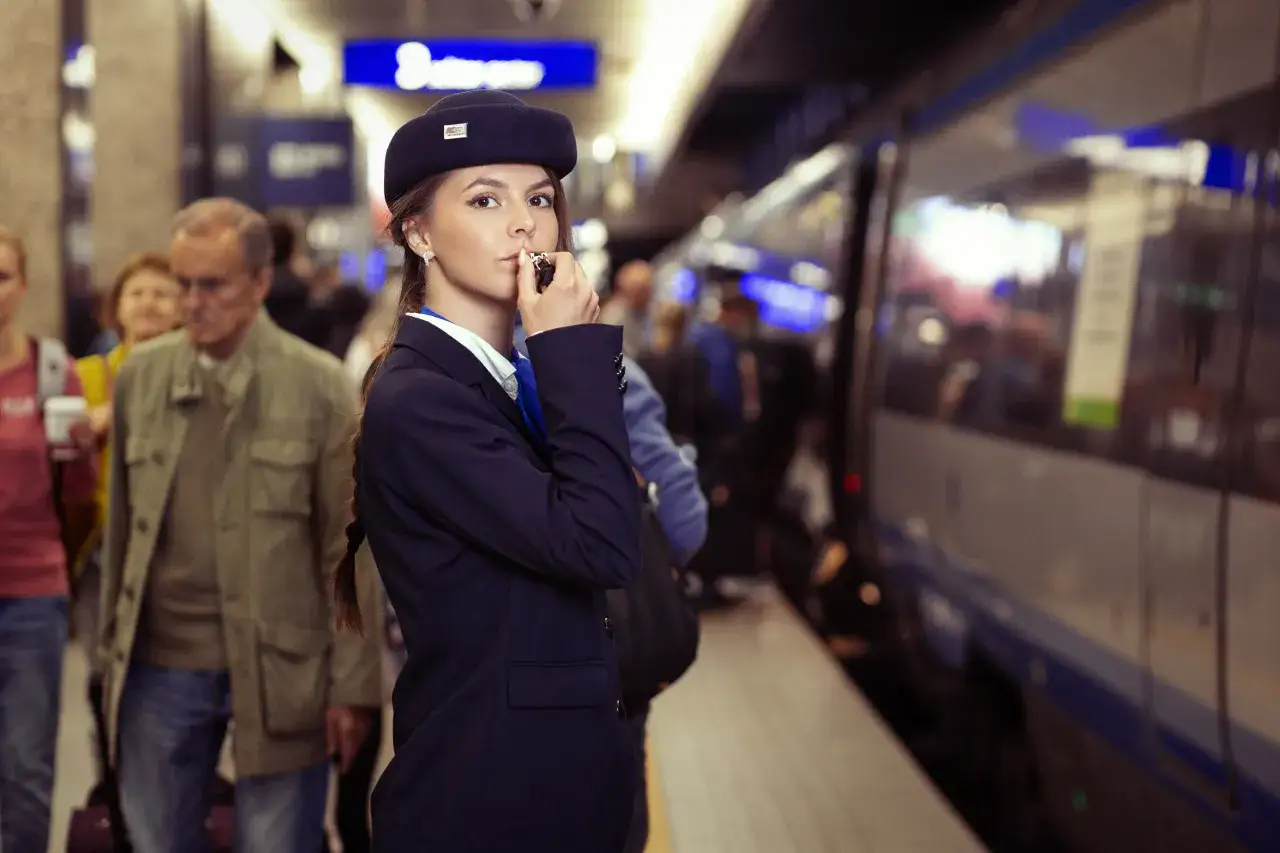 Młoda konduktorka w czapce z logo PKP Intercity, stojąca na peronie. Zastanawiasz się, ile zarabia konduktor Pendolino?